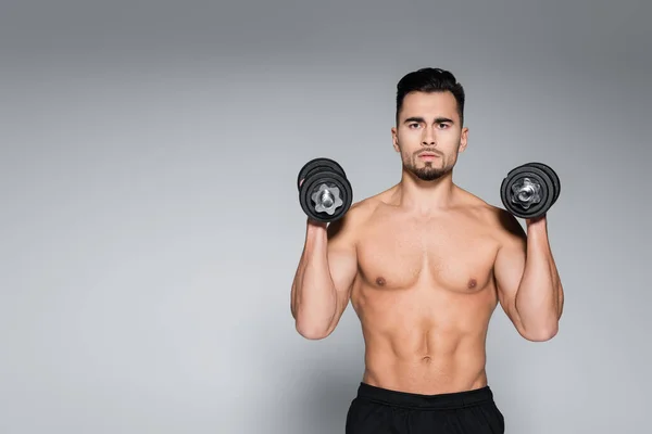 Deportista barbudo y musculoso haciendo ejercicio con mancuernas en gris - foto de stock