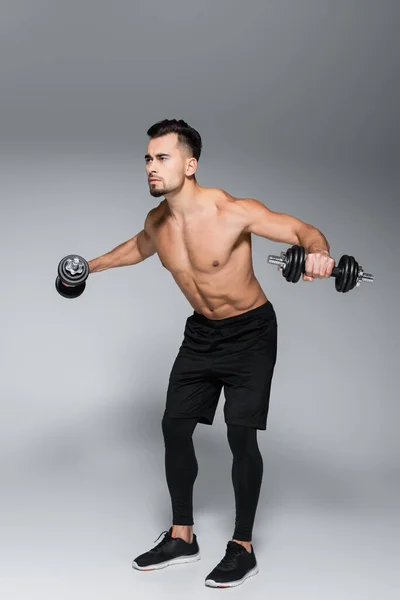 Full length of strong sportsman training with dumbbells on grey — Stock Photo
