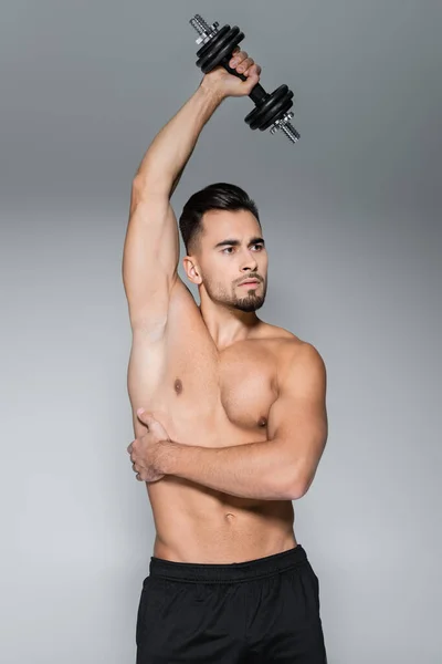 Strong sportsman training with dumbbell isolated on grey — Stock Photo