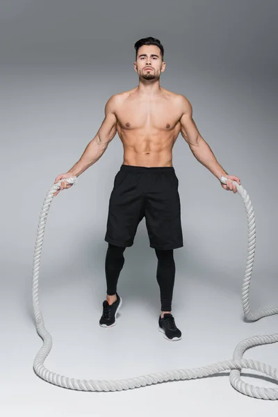 Full length of shirtless bearded man exercising with battle ropes on grey — Stock Photo