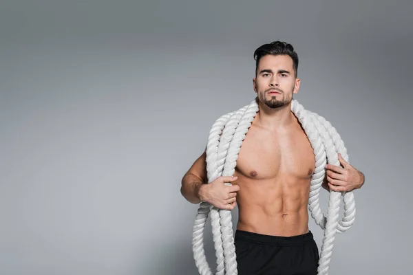 Без сорочки спортсмен тримає важкі бойові мотузки на плечах на сірому — стокове фото