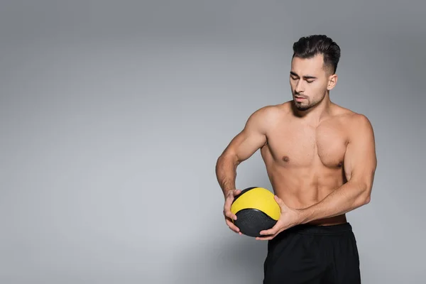 Deportista musculoso y barbudo mirando la pelota en gris - foto de stock