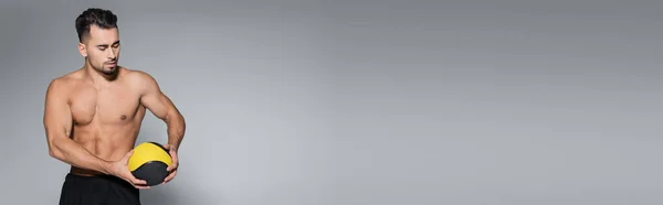 Sportif musclé et barbu regardant ballon sur gris, bannière — Photo de stock