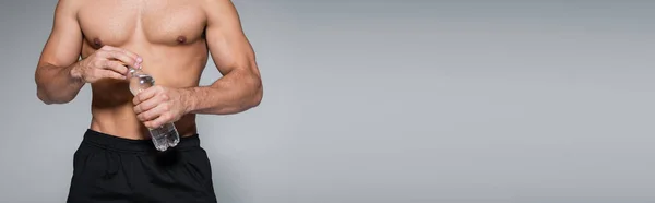 Vista recortada del deportista sin camisa sosteniendo la botella con agua aislada en gris, pancarta - foto de stock