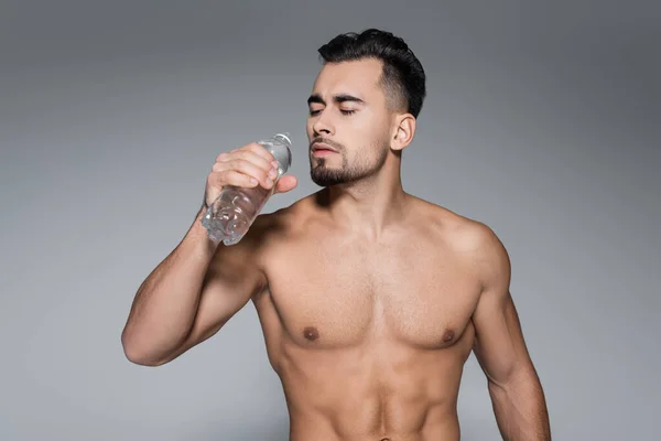 Muskulöser Sportler hält Flasche mit Wasser isoliert auf grau — Stockfoto