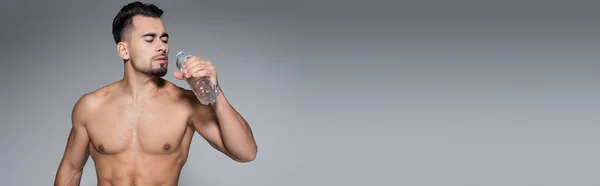 Hemdloser und muskulöser Sportler, der Flasche mit Wasser isoliert auf Grau hält, Banner — Stockfoto