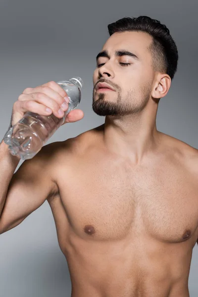 Desportista muscular segurando garrafa com água isolada em cinza — Fotografia de Stock