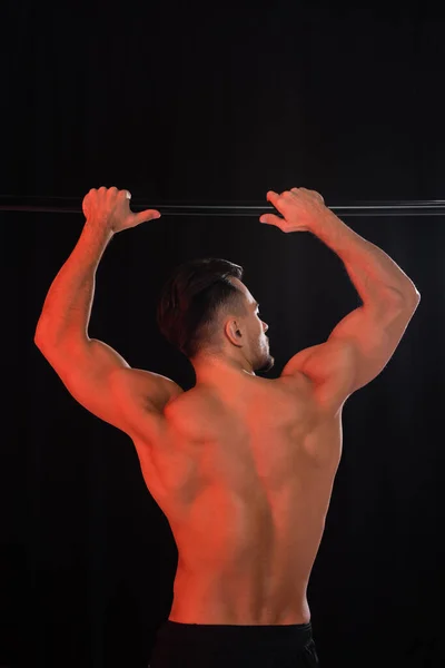 Back view of shirtless sportsman exercising on horizontal bar isolated on black — Stock Photo