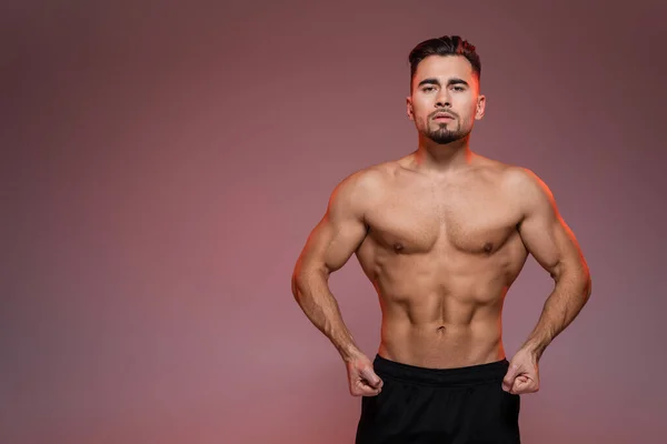 Red lighting on strong man with muscles posing on pink and grey — Stock Photo