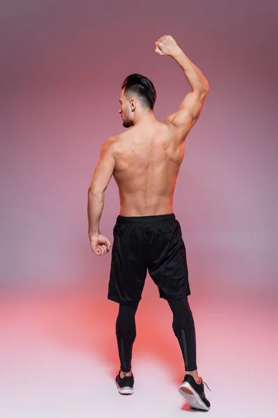 Вид сзади на безрубашечного человека, демонстрирующего мышцы и позирующего в розовом и сером — стоковое фото