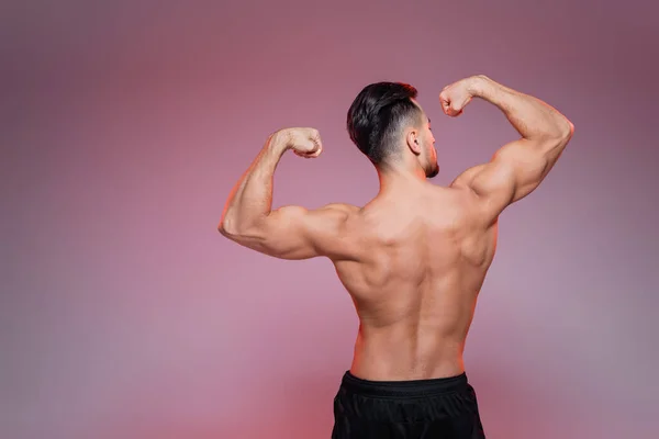 Back view of shirtless sportsman showing muscles on pink and grey — Stock Photo