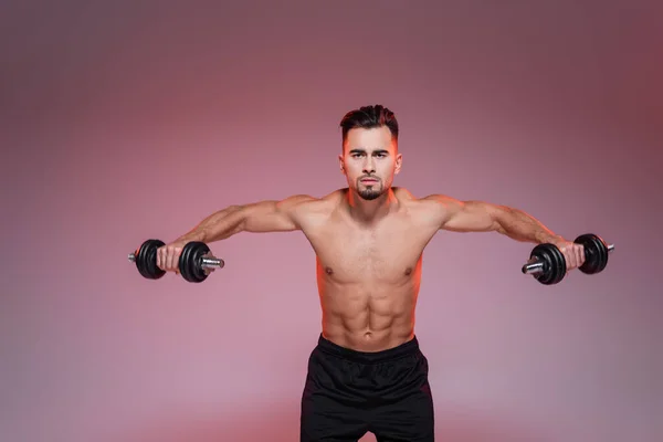 Мускулистый спортсмен тренируется с гантелями на розовом и сером — стоковое фото