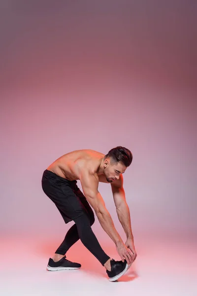 Shirtless sportsman leaning while stretching on grey and pink — Stock Photo