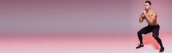 Comprimento total de desportista sem camisa fazendo exercício agachamento em cinza e rosa, banner — Fotografia de Stock