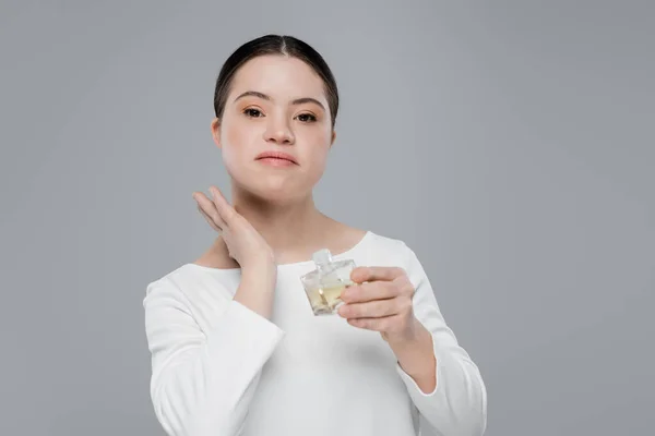 Young woman with down syndrome applying perfume isolated on grey — Stock Photo