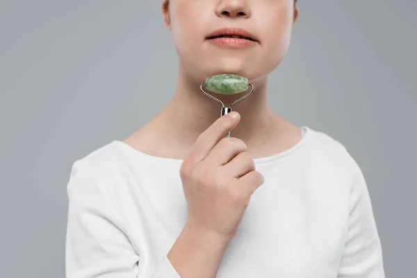 Cropped view of woman massaging chin with jade roller isolated on grey — Stock Photo