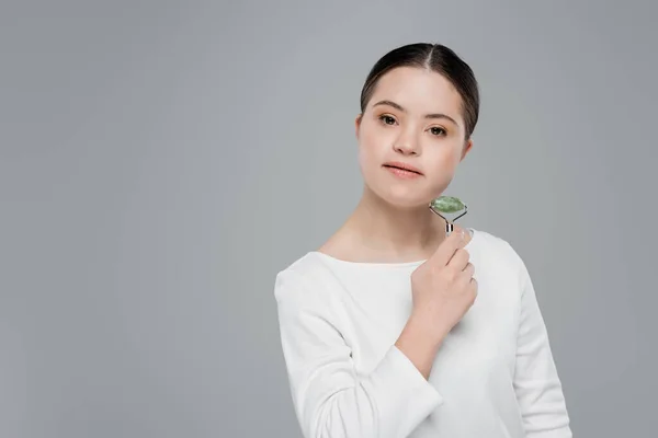 Young woman with down syndrome holding jade roller isolated on grey — Stock Photo