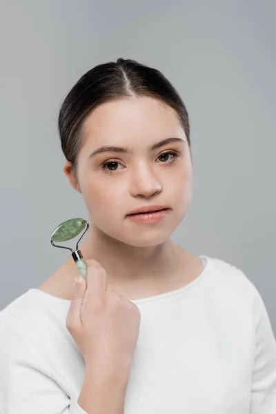 Young woman with down syndrome holding jade roller isolated on grey — Stock Photo