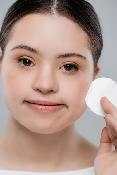 Young woman with down syndrome holding cotton pad isolated on grey — Stock Photo