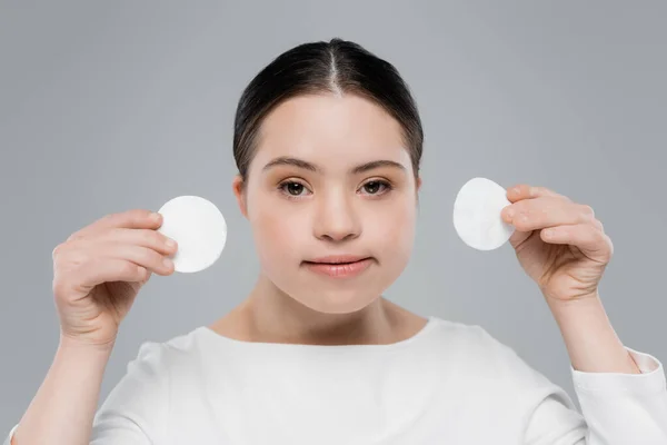 Junge Frau mit Down-Syndrom hält Wattepads isoliert auf grau — Stockfoto