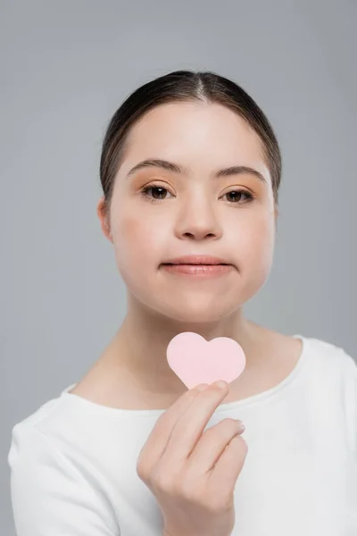 Junge Frau mit Down-Syndrom hält herzförmigen Schwamm isoliert auf grau — Stockfoto