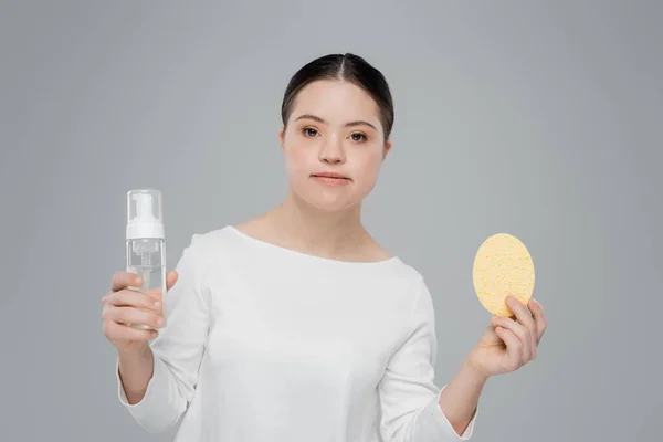 Mujer con síndrome de Down sosteniendo espuma limpiadora y esponja aislada en gris - foto de stock
