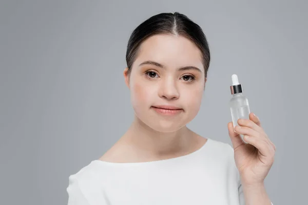 Молода жінка з синдромом Дауна тримає пляшку сироватки ізольовано на сірому — стокове фото