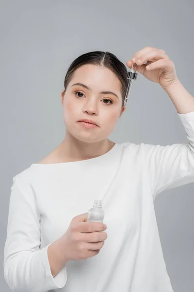 Woman with down syndrome holding cosmetic serum isolated on grey — Stock Photo