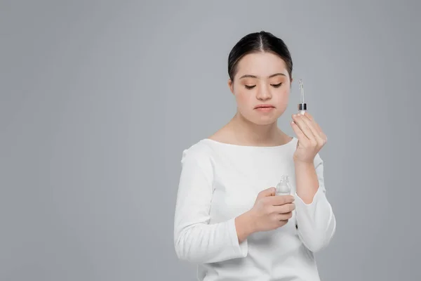 Young woman with down syndrome holding dropper and bottle of serum isolated on grey — Stock Photo