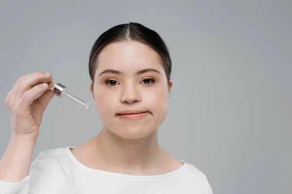 Woman with down syndrome holding dropper of cosmetic serum isolated on grey — Stock Photo