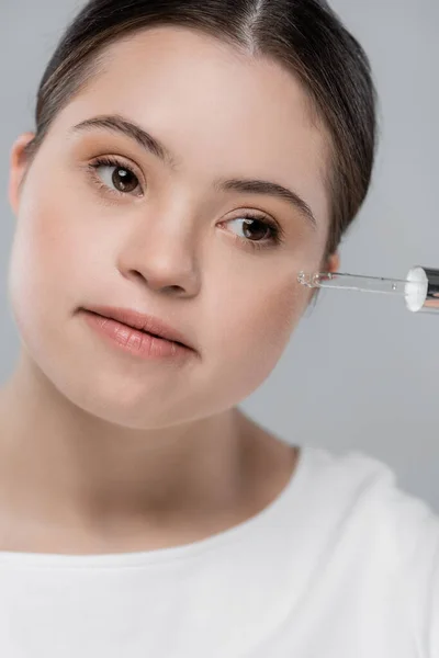 Porträt einer Frau mit Down-Syndrom, die Serum auf grau isoliert anwendet — Stockfoto