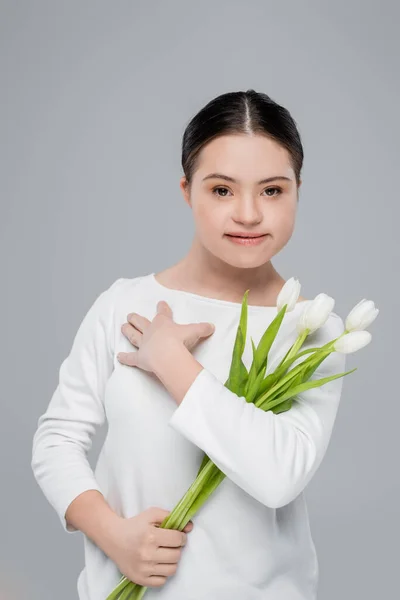 Mujer sonriente con síndrome de Down que sostiene tulipanes aislados en gris - foto de stock