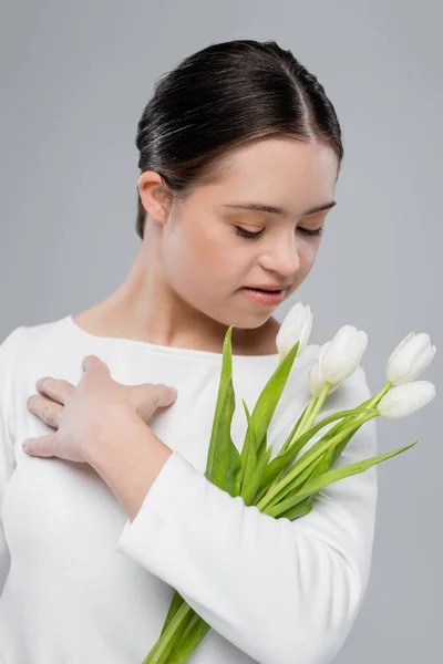 Junge Frau mit Down-Syndrom sieht Blumen isoliert auf grau — Stockfoto