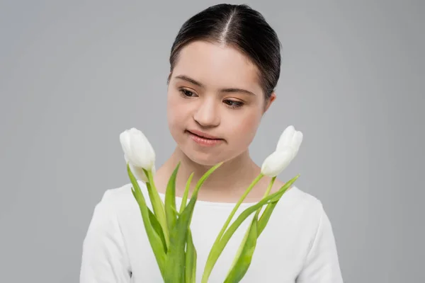 Mujer morena con síndrome de Down mirando flores aisladas en gris - foto de stock