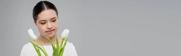 Mulher com síndrome de down olhando flores brancas isoladas em cinza, banner — Fotografia de Stock