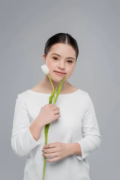 Mujer joven con síndrome de Down sosteniendo tulipán blanco aislado en gris - foto de stock