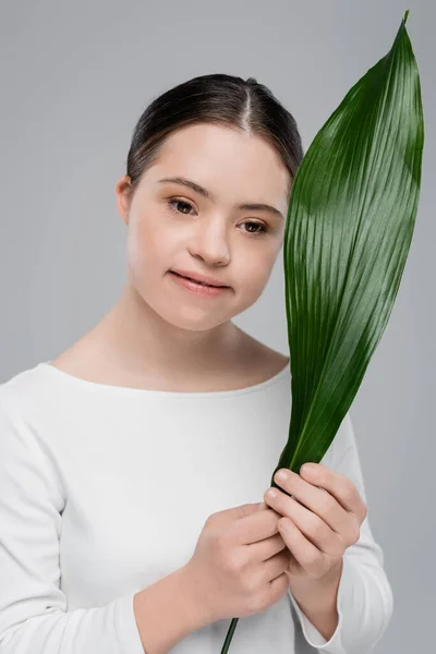 Smiling brunette woman with down syndrome holding leaf isolated on grey — Stock Photo