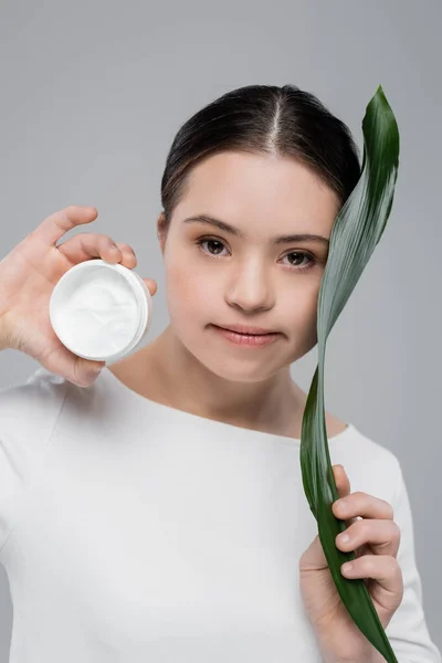 Frau mit Down-Syndrom hält Blatt und Kosmetikcreme isoliert auf grau — Stockfoto