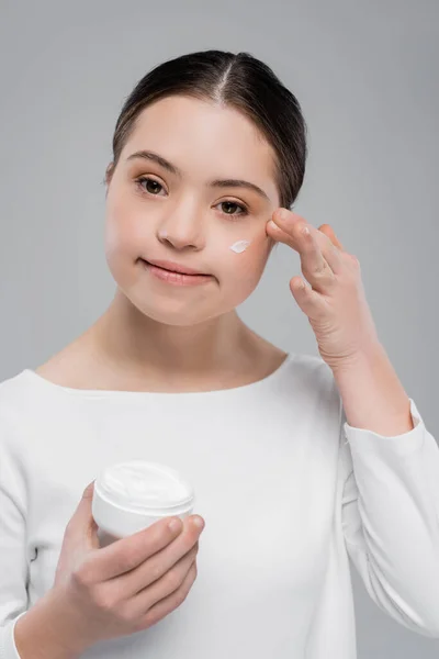 Молода жінка з синдромом Дауна наносить крем для обличчя ізольовано на сірий — стокове фото
