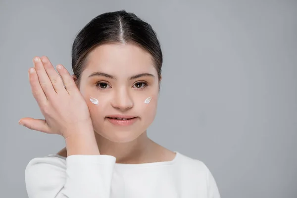 Positive Frau mit Down-Syndrom und Gesichtscreme isoliert auf grau — Stockfoto