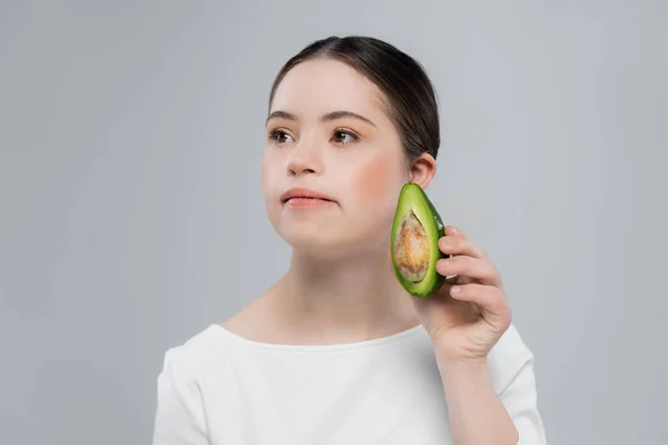 Mujer joven con síndrome de Down sosteniendo aguacate aislado en gris - foto de stock