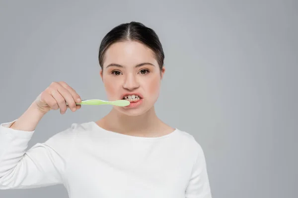 Woman with down syndrome brushing teeth isolated on grey — Stock Photo