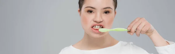 Junge Frau mit Down-Syndrom beim Zähneputzen isoliert auf grauem Banner — Stockfoto