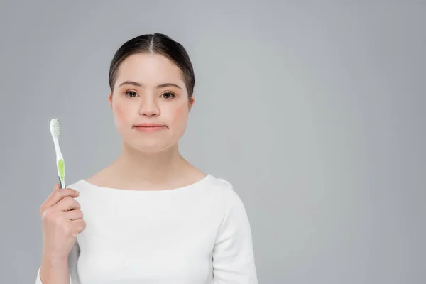 Mujer joven con síndrome de Down sosteniendo el cepillo de dientes y mirando a la cámara aislada en gris - foto de stock