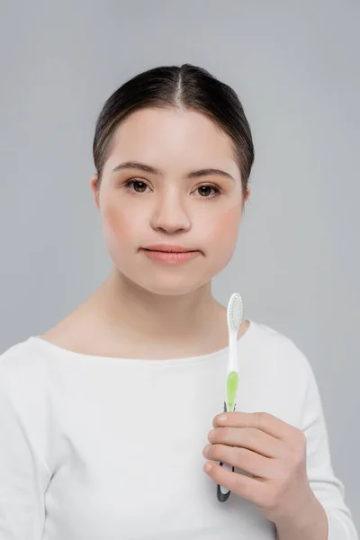 Mujer morena con síndrome de Down sosteniendo cepillo de dientes aislado en gris - foto de stock