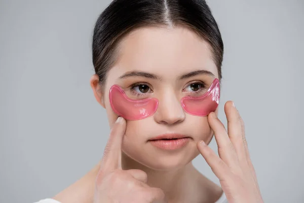 Mujer joven con síndrome de Down aplicando parches oculares aislados en gris - foto de stock