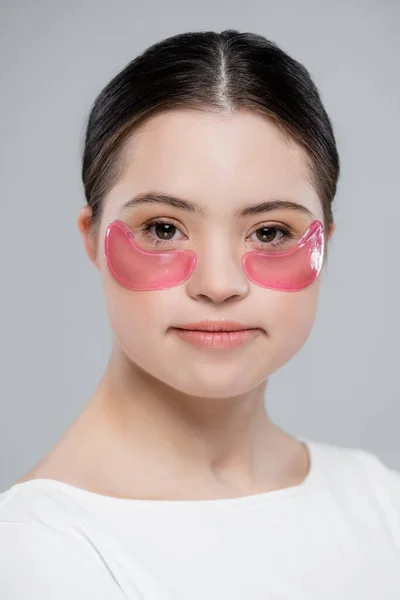 Портрет женщины с синдромом Дауна и повязками на глазу, смотрящей на камеру, изолированную на сером — стоковое фото