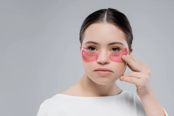 Young woman with down syndrome applying eye patches isolated on grey — Stock Photo