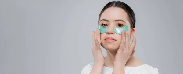 Woman with down syndrome applying hydrogel eye patches isolated on grey, banner — Stock Photo