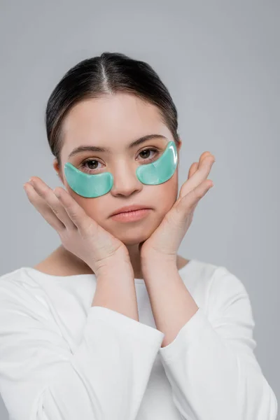 Portrait de jeune femme atteinte du syndrome du duvet et des bandeaux oculaires touchant le visage isolé sur le gris — Photo de stock